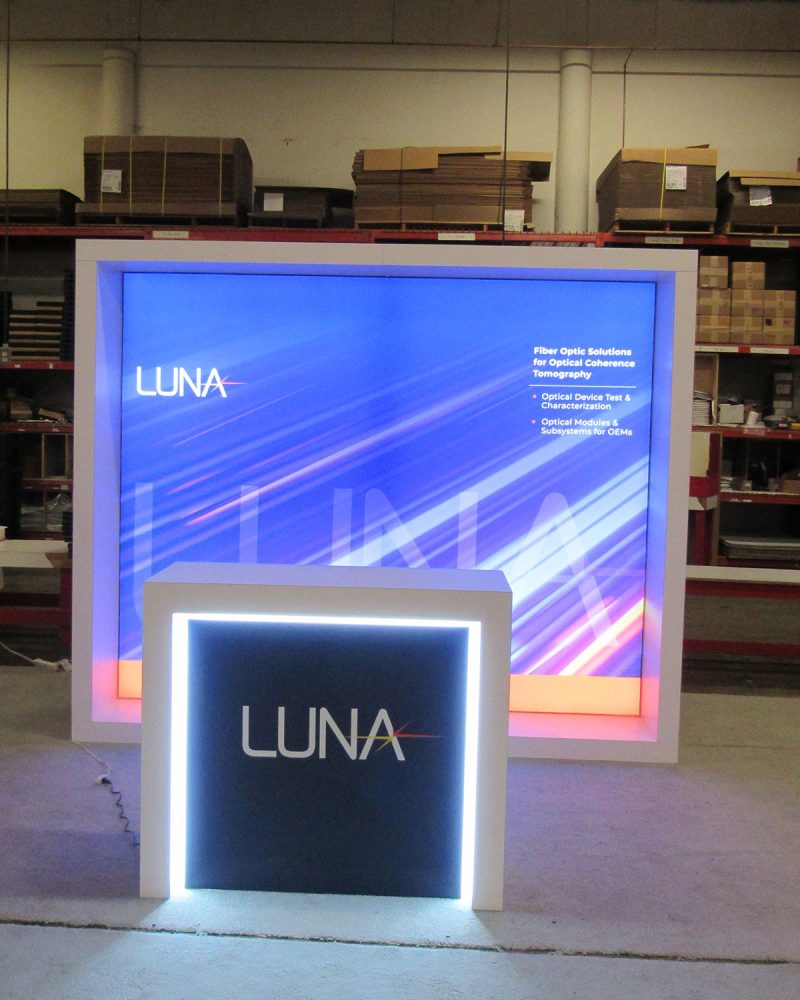 Example 10’ Custom laminate exhibit design featuring wood construction laminated shadowbox framing the backlit graphic perimeter and large counter with edge glow